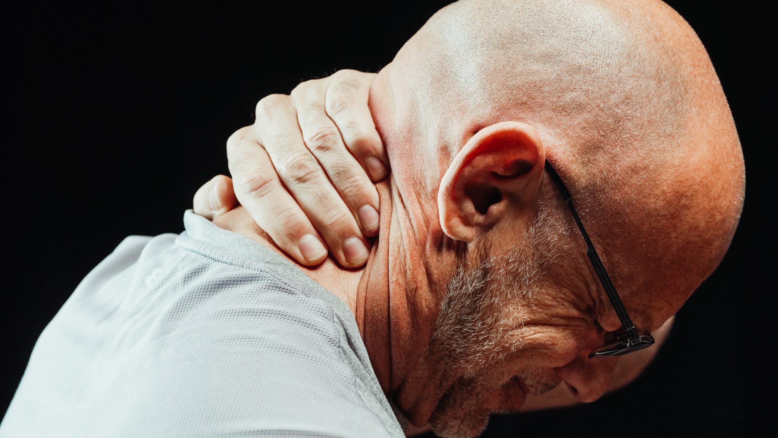 An older man grabbing the back of his neck and is visibly in pain.