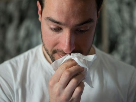 closeup of a man with a red nose and tissue in his hand.